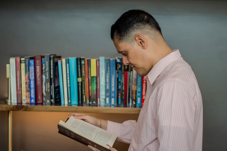 Rolando López leyendo un libro junto a una estantería.